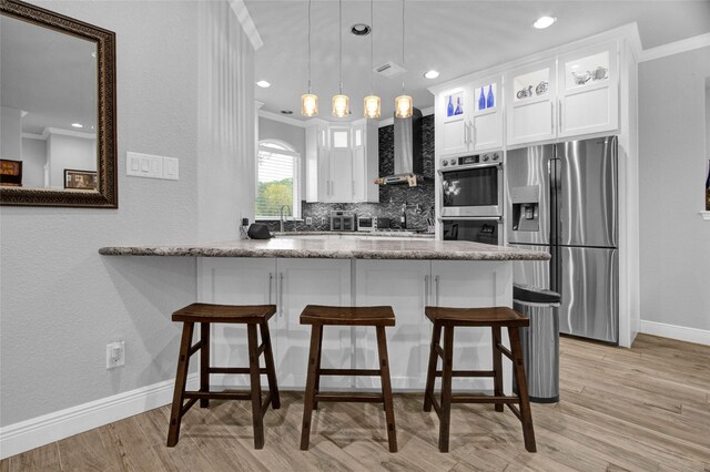 kitchen with white cabinetry, wall chimney exhaust hood, hanging light fixtures, decorative backsplash, and appliances with stainless steel finishes