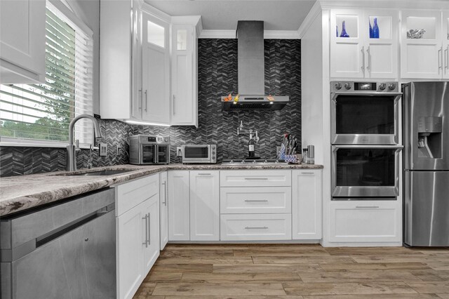 kitchen with light stone countertops, white cabinetry, appliances with stainless steel finishes, and wall chimney range hood