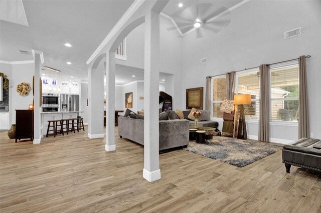 living room with ceiling fan, light hardwood / wood-style floors, a high ceiling, and ornamental molding