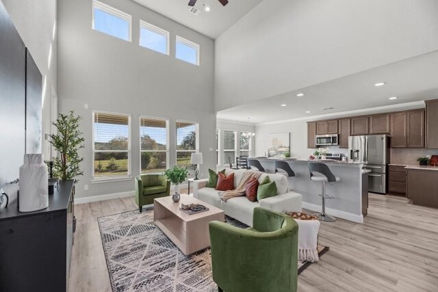 living room featuring light wood-type flooring, a towering ceiling, ceiling fan with notable chandelier, and plenty of natural light