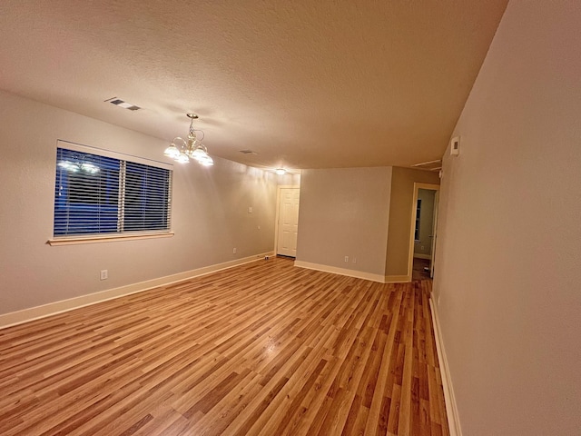 spare room featuring an inviting chandelier, a textured ceiling, and hardwood / wood-style flooring