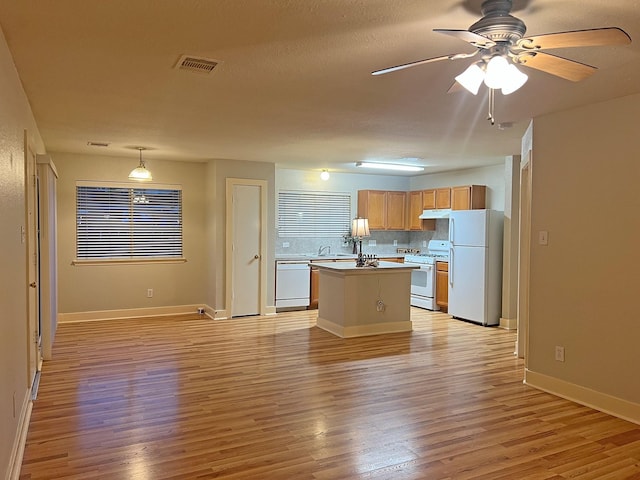 kitchen featuring light wood-type flooring, backsplash, white appliances, sink, and a kitchen island