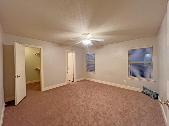 unfurnished bedroom with carpet, a textured ceiling, ceiling fan, a spacious closet, and a closet