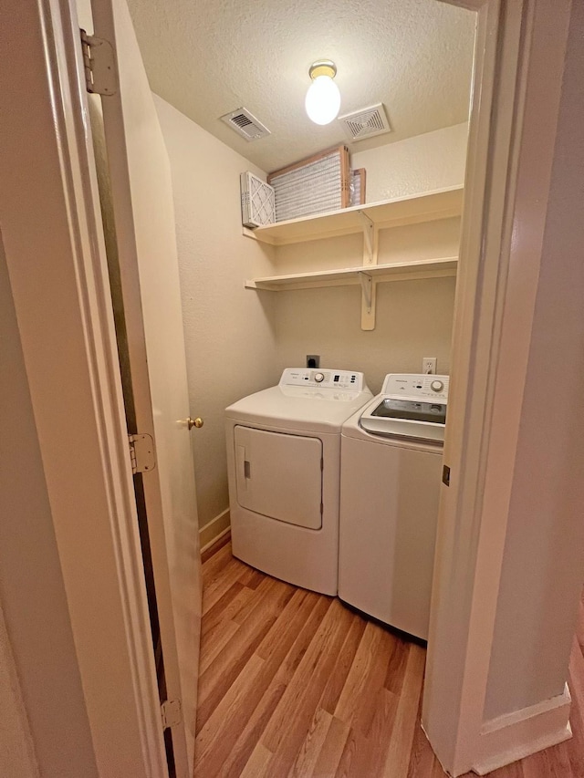 laundry area with separate washer and dryer, light hardwood / wood-style flooring, and a textured ceiling