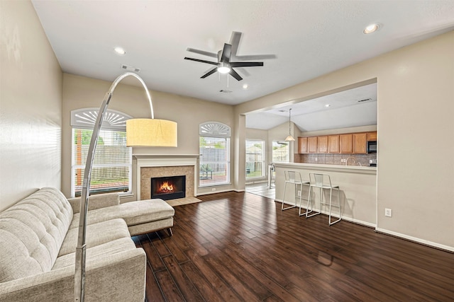 living room featuring wood-type flooring, vaulted ceiling, ceiling fan, and a tiled fireplace