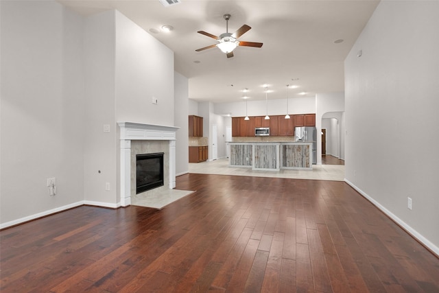 unfurnished living room featuring a tile fireplace, hardwood / wood-style floors, and ceiling fan