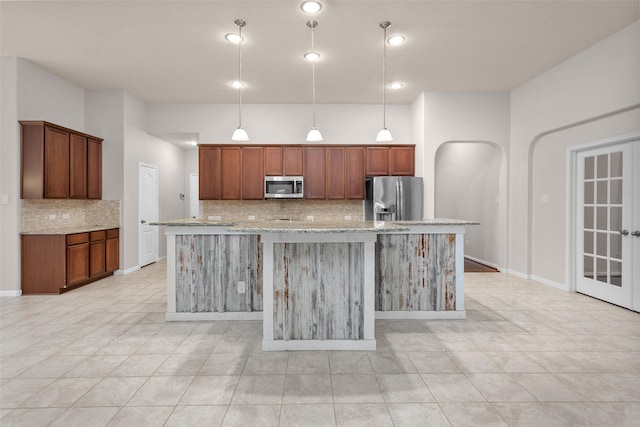 kitchen featuring hanging light fixtures, light stone countertops, a kitchen island with sink, and appliances with stainless steel finishes