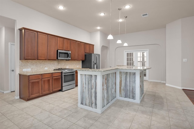 kitchen with hanging light fixtures, tasteful backsplash, light stone counters, a center island with sink, and appliances with stainless steel finishes