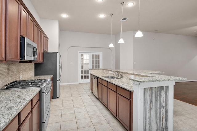 kitchen featuring sink, hanging light fixtures, light stone counters, light hardwood / wood-style floors, and appliances with stainless steel finishes