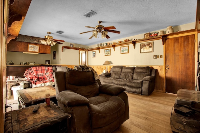 living room with a textured ceiling, light wood-type flooring, ceiling fan, and wood walls