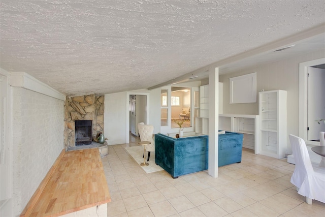 unfurnished living room featuring a stone fireplace, light tile patterned floors, and a textured ceiling