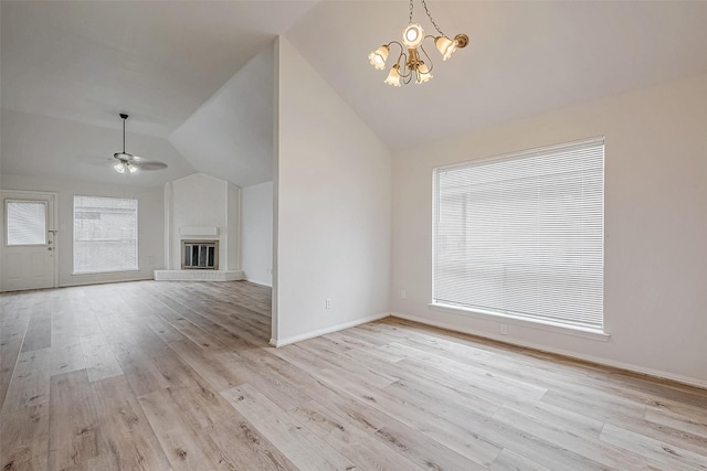 unfurnished living room featuring baseboards, a glass covered fireplace, vaulted ceiling, light wood-type flooring, and ceiling fan with notable chandelier