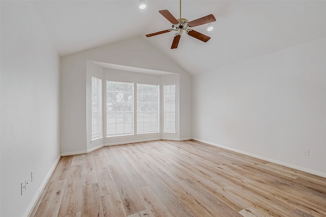 empty room featuring lofted ceiling, light wood finished floors, baseboards, and a ceiling fan