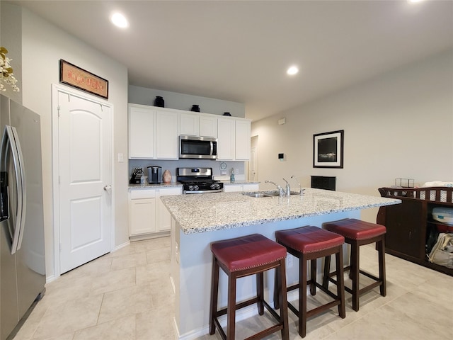 kitchen with sink, an island with sink, a kitchen bar, white cabinetry, and stainless steel appliances