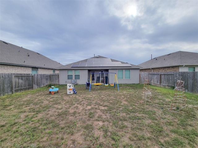 rear view of house featuring solar panels, a playground, and a lawn