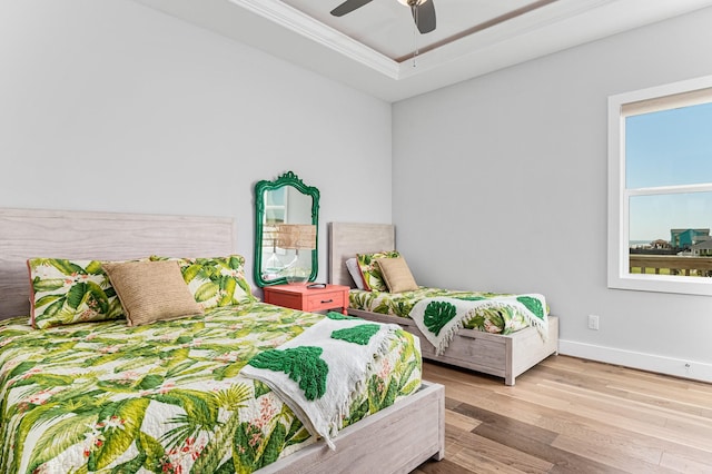 bedroom featuring a tray ceiling, ceiling fan, ornamental molding, and light wood-type flooring