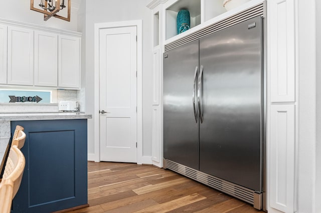 kitchen featuring backsplash, stainless steel built in refrigerator, dark wood-type flooring, a chandelier, and white cabinetry