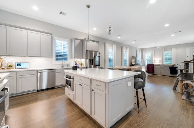 kitchen with a center island, stainless steel appliances, tasteful backsplash, wood-type flooring, and decorative light fixtures