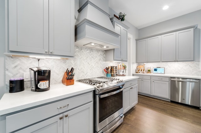 kitchen featuring gray cabinetry, custom exhaust hood, backsplash, hardwood / wood-style flooring, and stainless steel appliances