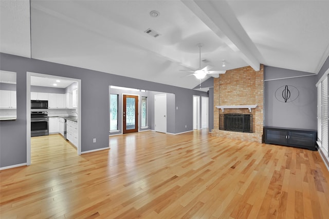 unfurnished living room featuring vaulted ceiling with beams, light hardwood / wood-style floors, ceiling fan, and a brick fireplace