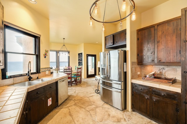 kitchen with appliances with stainless steel finishes, dark brown cabinets, sink, pendant lighting, and tile counters