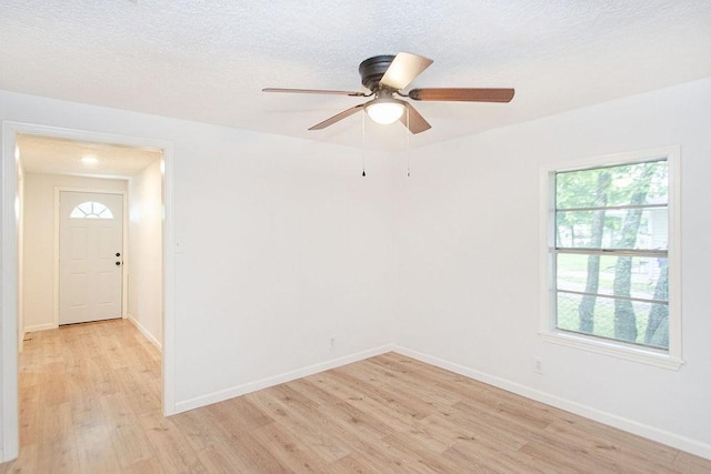 empty room featuring a textured ceiling, ceiling fan, light hardwood / wood-style flooring, and plenty of natural light