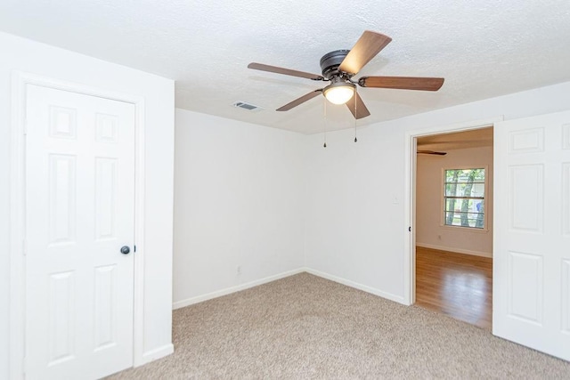 empty room featuring a textured ceiling, ceiling fan, and light colored carpet