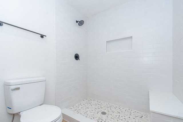 bathroom with a tile shower and toilet