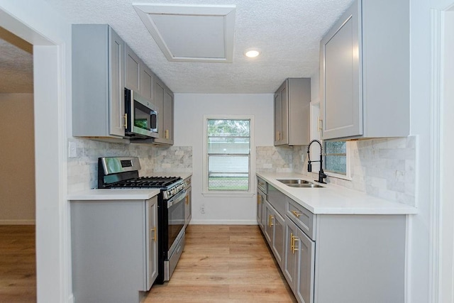 kitchen with a textured ceiling, light wood-type flooring, gray cabinets, appliances with stainless steel finishes, and sink