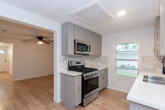 kitchen with stainless steel appliances, tasteful backsplash, gray cabinetry, and light hardwood / wood-style flooring