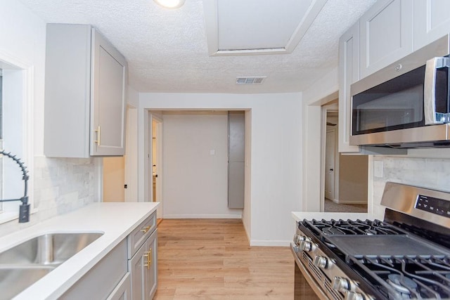 kitchen with sink, a textured ceiling, light wood-type flooring, backsplash, and appliances with stainless steel finishes