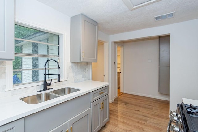 kitchen featuring gas range, light hardwood / wood-style floors, tasteful backsplash, gray cabinets, and sink