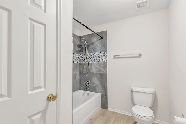 bathroom with hardwood / wood-style floors, toilet, and tiled shower / bath