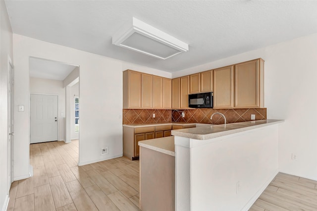 kitchen with backsplash, kitchen peninsula, a textured ceiling, and light wood-type flooring