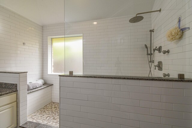 bathroom featuring tiled shower, vanity, and tile walls