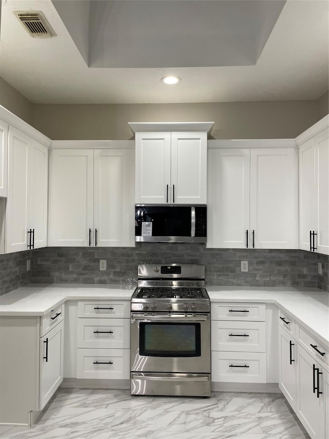 kitchen with backsplash, white cabinets, and stainless steel appliances