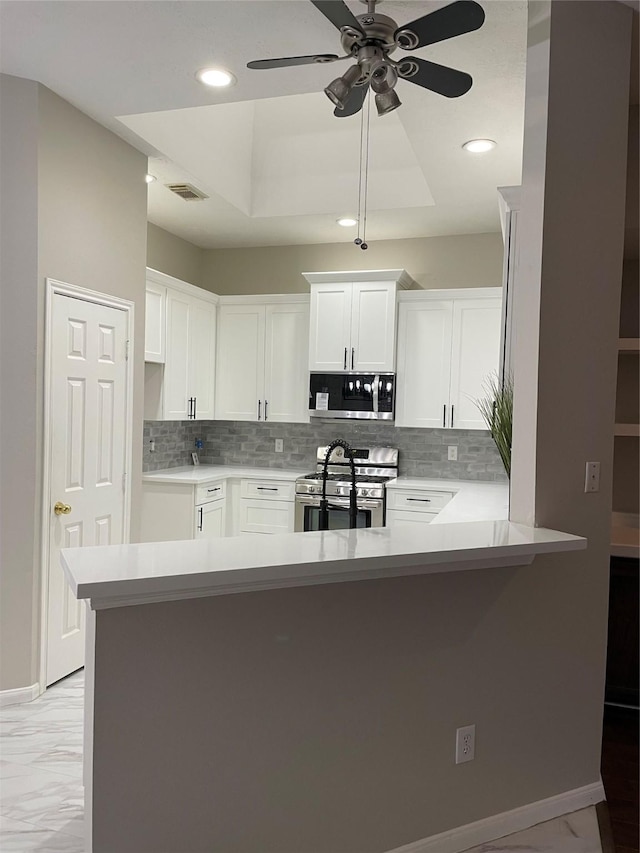 kitchen featuring a raised ceiling, kitchen peninsula, white cabinets, and appliances with stainless steel finishes