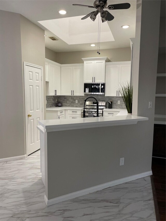 kitchen featuring appliances with stainless steel finishes, kitchen peninsula, a raised ceiling, and white cabinets