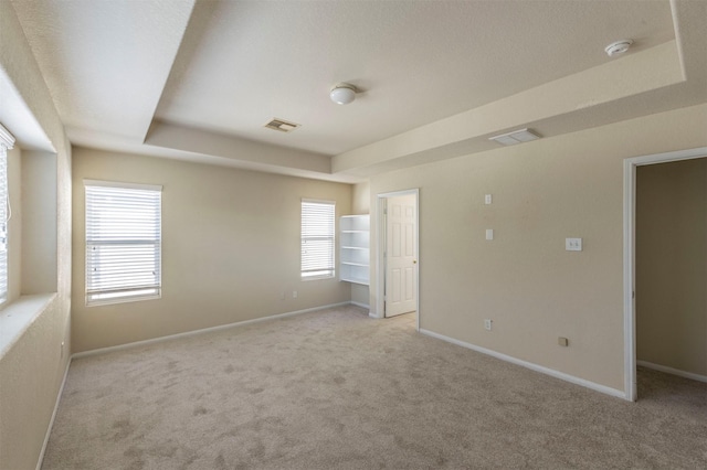 unfurnished room featuring a textured ceiling, a raised ceiling, and light carpet