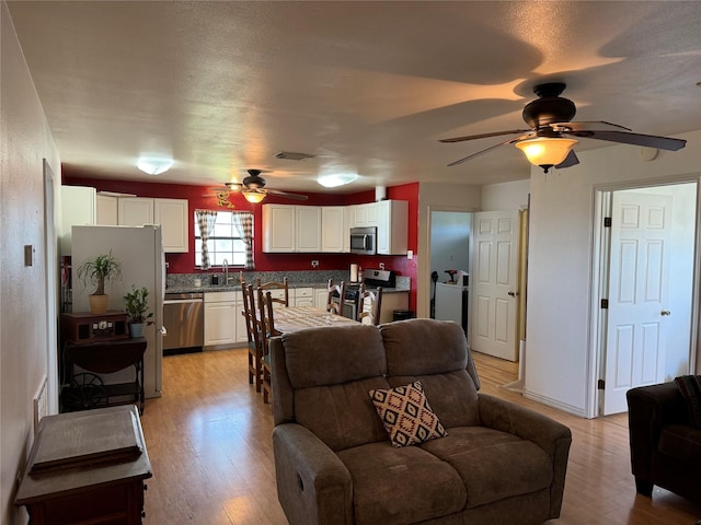 living room with a textured ceiling, light wood-type flooring, ceiling fan, and sink