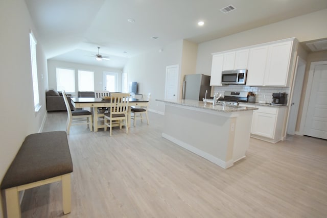 kitchen with ceiling fan, vaulted ceiling, a center island with sink, white cabinets, and appliances with stainless steel finishes