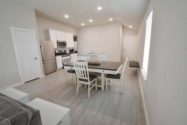 dining area with light hardwood / wood-style floors, vaulted ceiling, a healthy amount of sunlight, and sink