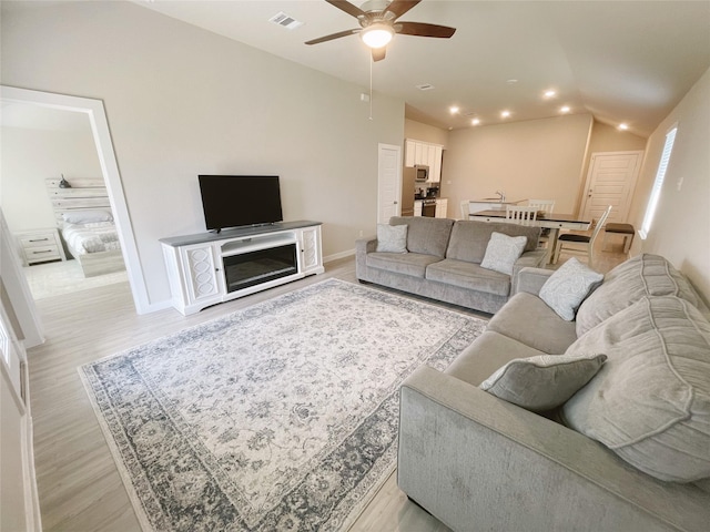 living room featuring ceiling fan, lofted ceiling, and light wood-type flooring