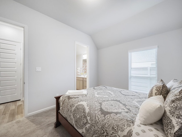 carpeted bedroom featuring ensuite bath and vaulted ceiling