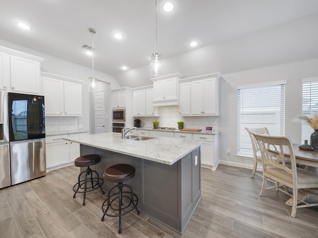 kitchen with stainless steel appliances, sink, a center island with sink, white cabinetry, and hanging light fixtures