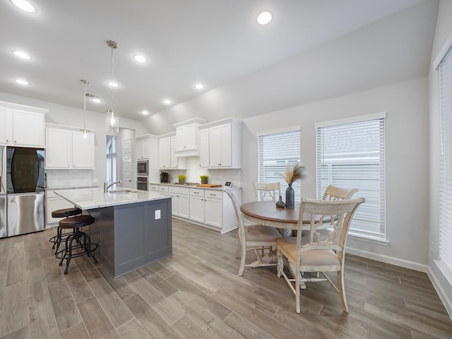 kitchen featuring white cabinetry, pendant lighting, lofted ceiling, light hardwood / wood-style floors, and a kitchen island with sink