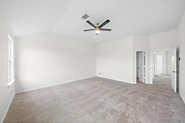 empty room with a wealth of natural light, ceiling fan, light colored carpet, and vaulted ceiling