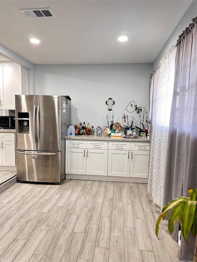 kitchen with light stone counters, white cabinets, stainless steel refrigerator with ice dispenser, and light wood-type flooring