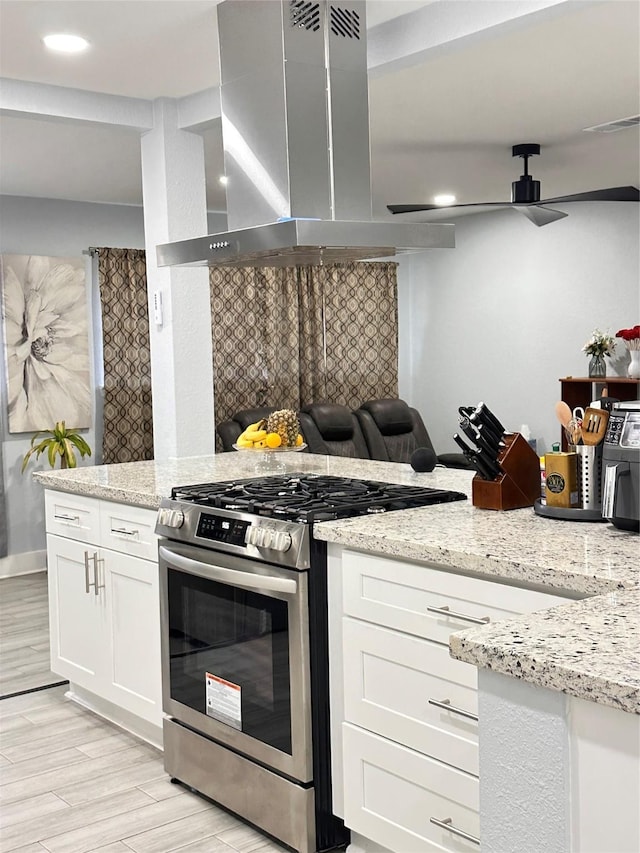 kitchen featuring light stone countertops, wall chimney exhaust hood, gas stove, light hardwood / wood-style flooring, and white cabinets