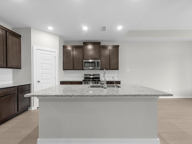 kitchen with sink, appliances with stainless steel finishes, a kitchen island with sink, and dark brown cabinets